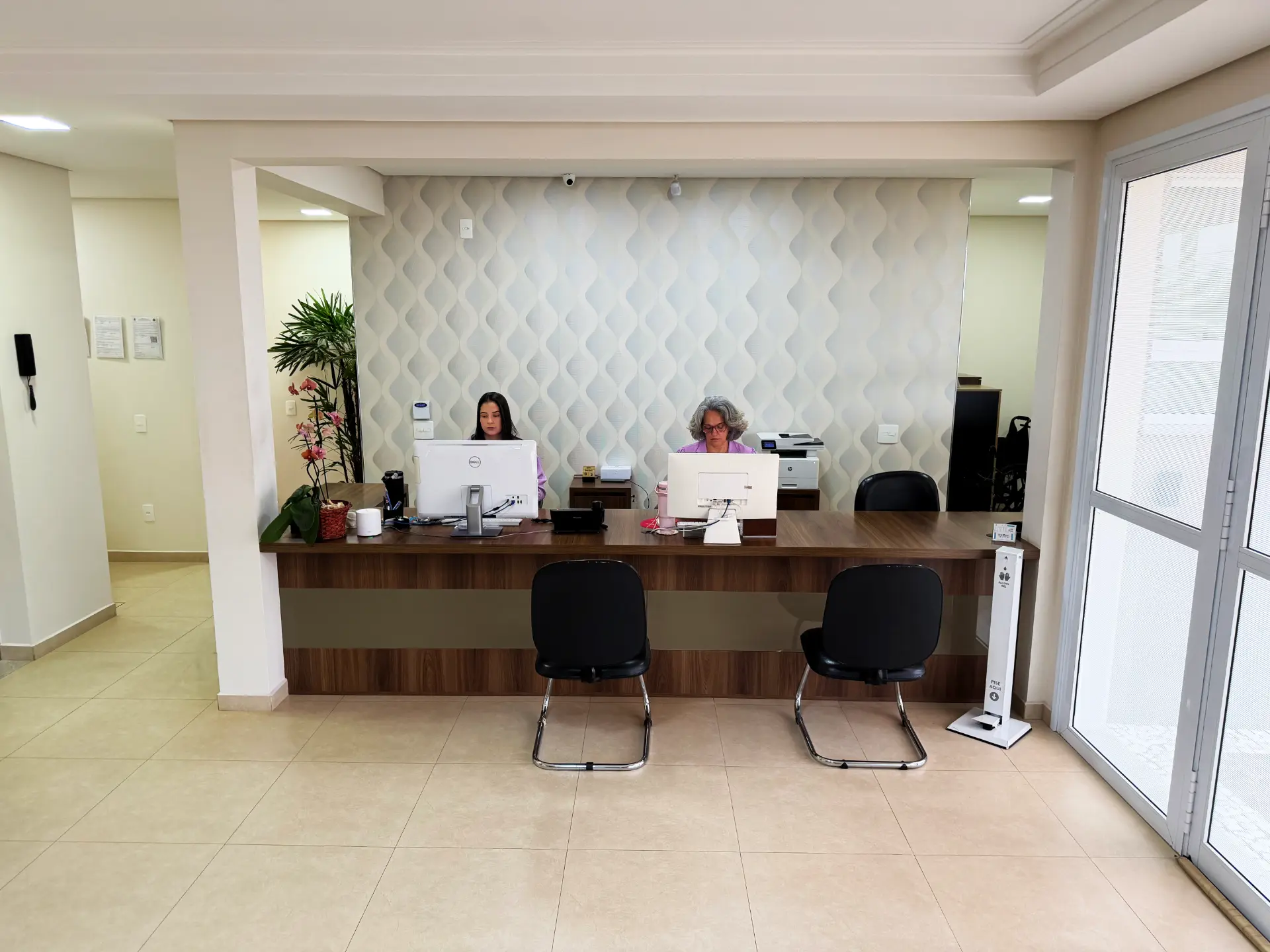 Recepção da Clínica Revita com balcão de atendimento, plantas e duas recepcionistas